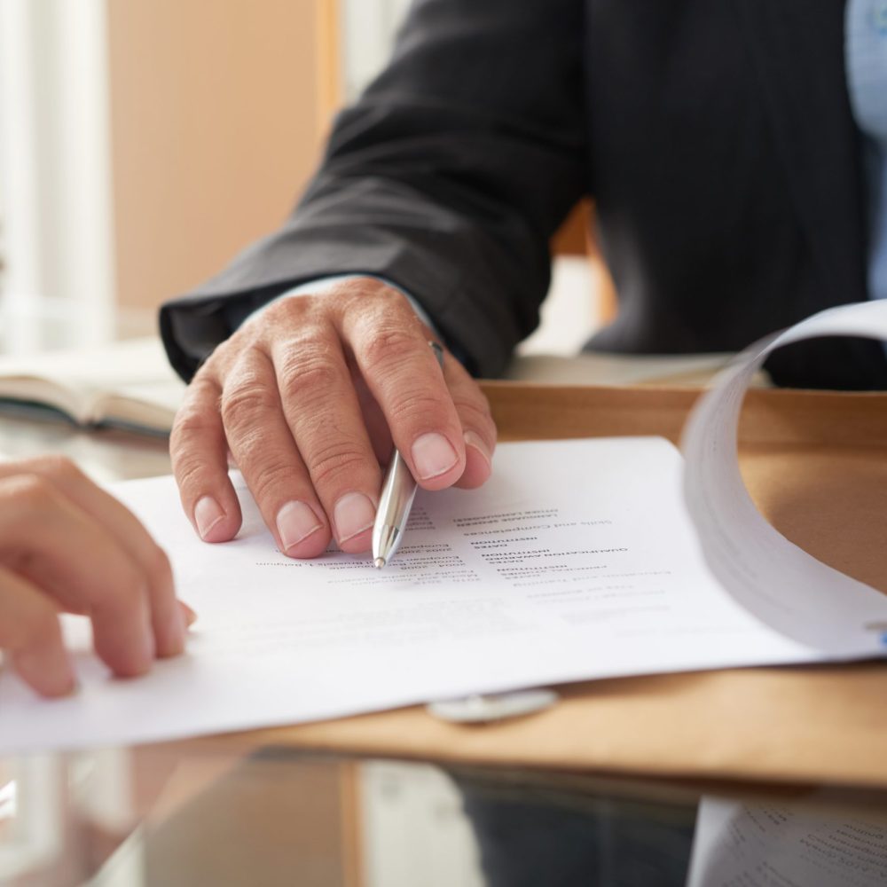 Business people signing a contract Close-up of businessman examining business contract and signing it at the office desk